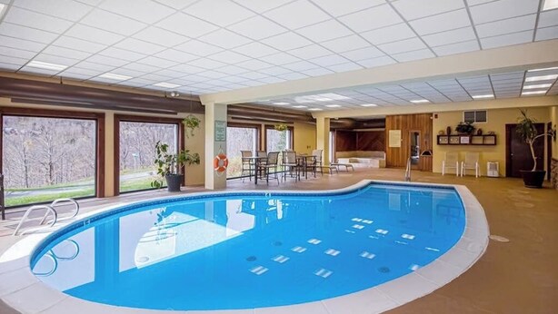 Ein Hallenbad mit Fliesenboden, einer Poolleiter und einem Sitzbereich mit Stühlen und Tischen.