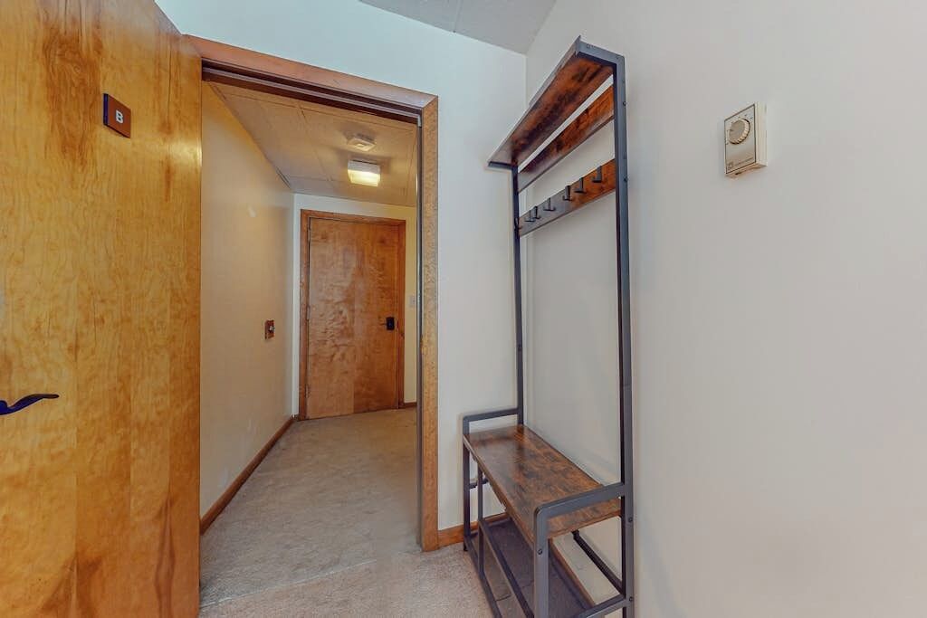 A hallway with a wooden door, a metal bench, and a coat rack.