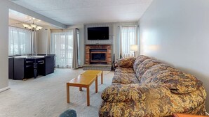 Ein Wohnzimmer mit Sofa, Fernseher, Kamin und Schreibtisch mit Stuhl.