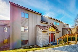 Ein mehrstöckiges Gebäude mit Garage, einem kleinen Anbau mit roter Tür und einer Holzrampe, die zum Eingang führt.