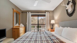 A bedroom with a bed, a dresser, a television, a ceiling fan, a balcony with a view, and a deer head decoration. - Slopeside condo with nearby skiing, balcony, fireplace, & washer/dryer (Dover)