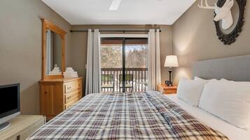 A bedroom with a bed, a dresser, a television, a ceiling fan, a balcony with a view, and a deer head decoration.