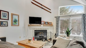 A living room with a fireplace, a television, and a large window with curtains. - Slopeside condo with nearby skiing, balcony, fireplace, & washer/dryer (Dover)