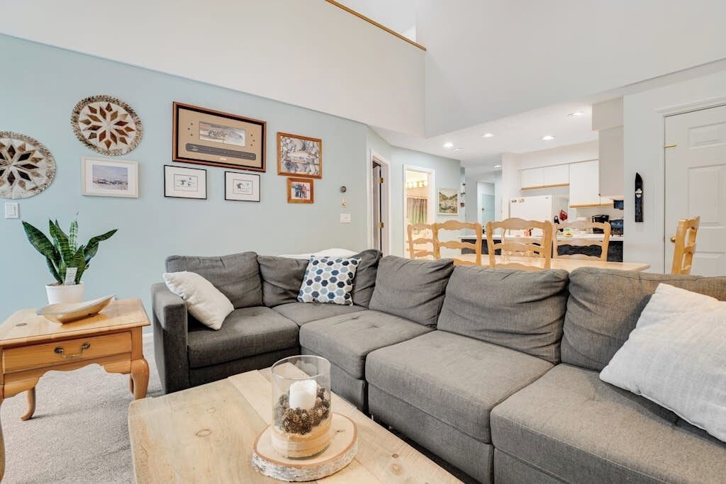 A living room with a grey sectional sofa, a wooden coffee table, and a dining area with a wooden table and chairs.