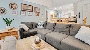 A living room with a grey sectional sofa, a wooden coffee table, and a dining area with a wooden table and chairs. - Slopeside condo with nearby skiing, balcony, fireplace, & washer/dryer (Dover)