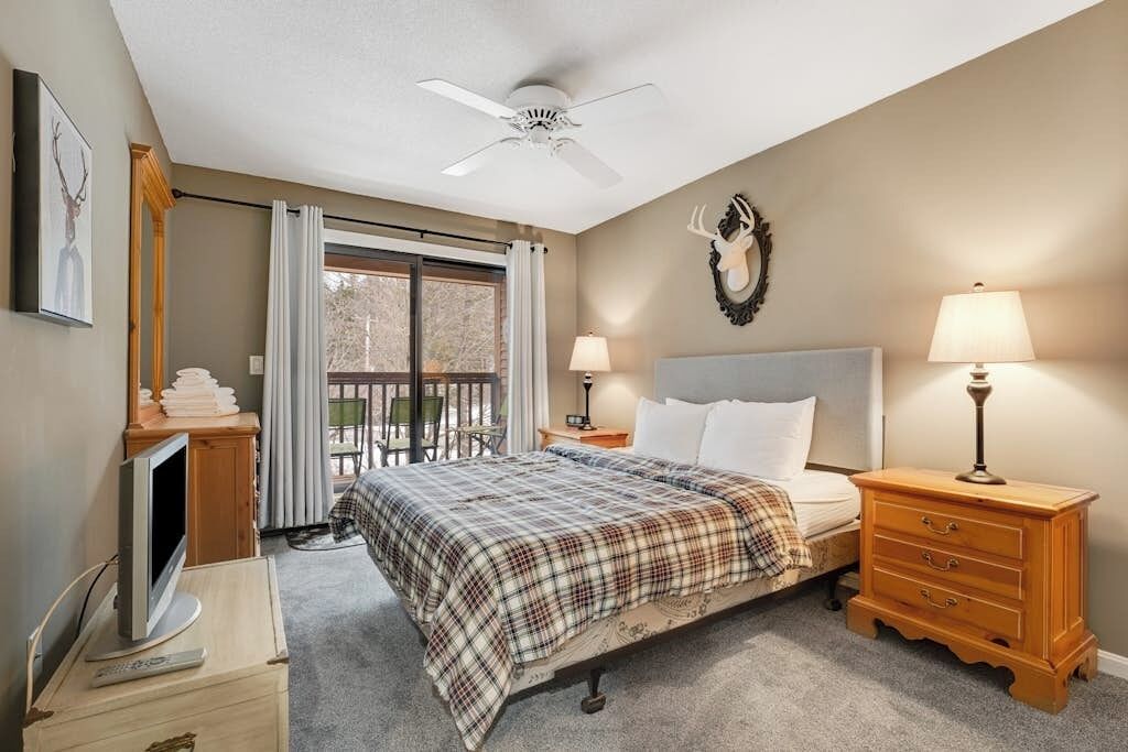 Une chambre à coucher comprenant un lit, un ventilateur de plafond, une tête de cerf montée au mur, un téléviseur et un balcon avec une chaise.