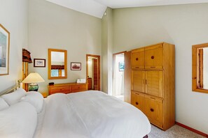 Ein Hotelzimmer mit einem Bett, einem Holzschrank, einem Schreibtisch mit Lampe und gerahmten Bildern an der Wand.