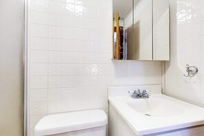 Ein Badezimmer mit weißen Fliesen, einer weißen Toilette, einem Waschbecken mit Wasserhahn und einem Spiegel darüber.
