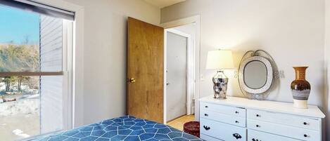 Un dormitorio con cama, cómoda, espejo y puerta que da a otra habitación.