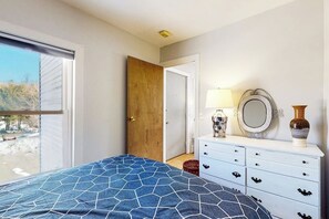 Ein Schlafzimmer mit einem Bett, einer Kommode, einem Spiegel und einer Tür zu einem anderen Raum.