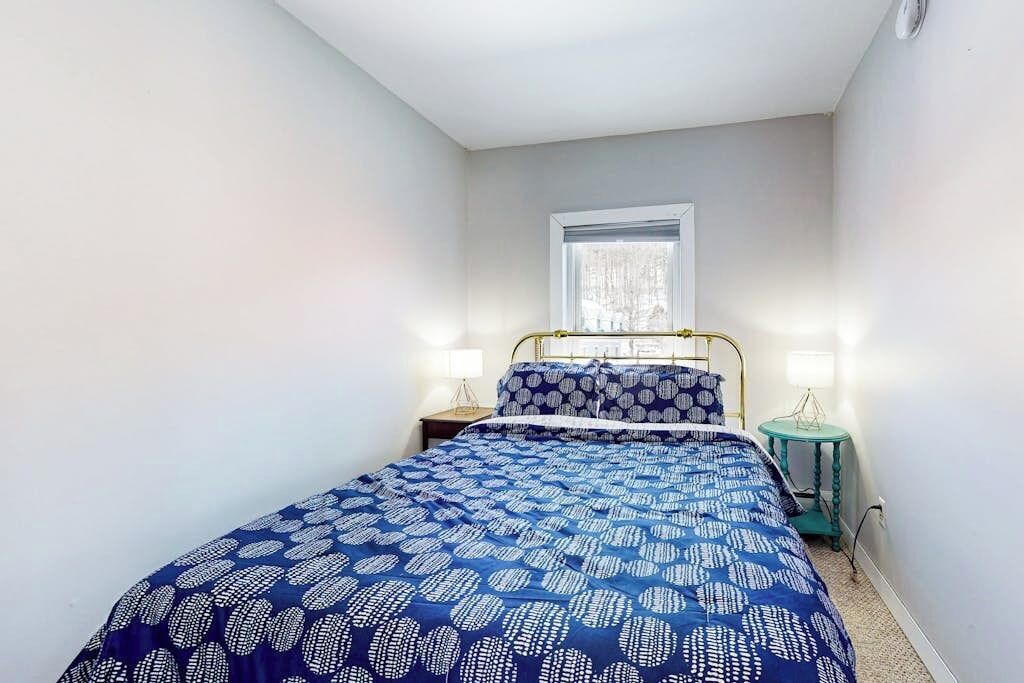 Ein Schlafzimmer mit einem Bett, zwei Nachttischen, einem Fenster und einem kleinen Tisch.