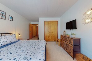 Un dormitorio con cama, cómoda, televisor y un pasillo que conduce a otra habitación.
