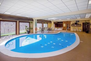An indoor swimming pool with a tiled floor, a pool ladder, and a seating area with chairs and tables.