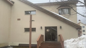 A building with a wooden staircase leading to a door, a small window, and a snow-covered ground. - Cozy retreat near slopes (Dover)