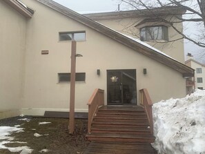 A building with a wooden staircase leading to a door, a small window, and a snow-covered ground. - Cozy retreat near slopes (Dover)