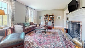 A living room with a fireplace, a sofa, a coffee table, a bookshelf, and a television mounted on the wall.