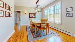 A dining area with a wooden table and chairs, a patterned rug, and framed pictures on the walls.