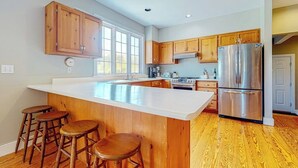 A kitchen with wooden cabinets, a stainless steel refrigerator, a large island with stools, and a window.