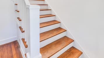 Un escalier avec des marches en bois et des rampes blanches, menant à un palier où se trouve un paillasson.