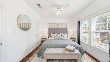 Een slaapkamer met een bed, een ronde spiegel, een plafondventilator en een raam met jaloezieën.