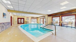 Una piscina interior con suelo de baldosas, un reloj en la pared y vistas a un paisaje nevado a través de amplias ventanas.