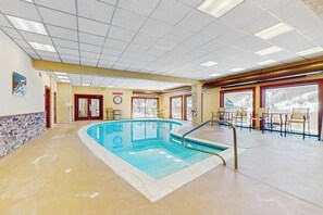 An indoor swimming pool with a tiled floor, a clock on the wall, and a view of a snowy landscape through large windows. - Comfortable condo with fireplace, pool, and sauna access - near slopes (Dover)