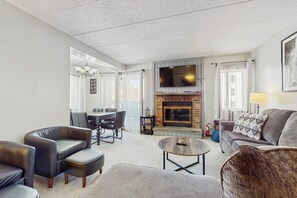 A modern living room with a fireplace, a flat-screen TV, and a dining area. - Comfortable condo with fireplace, pool, and sauna access - near slopes (Dover)