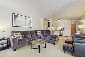 A living room with a sectional sofa, a round coffee table, and a kitchen in the background. - Comfortable condo with fireplace, pool, and sauna access - near slopes (Dover)