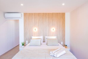 Ein modernes Hotelzimmer mit einem großen Bett, zwei Nachttischen, einer Wandklimaanlage und zwei Wandleuchten.