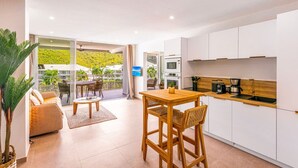 A modern kitchen with white cabinets, a wooden dining table, and a balcony with a view of a green hillside. - Serenity Bay – Prestige Suite Anse Marcel beach front (Anse Marcel)