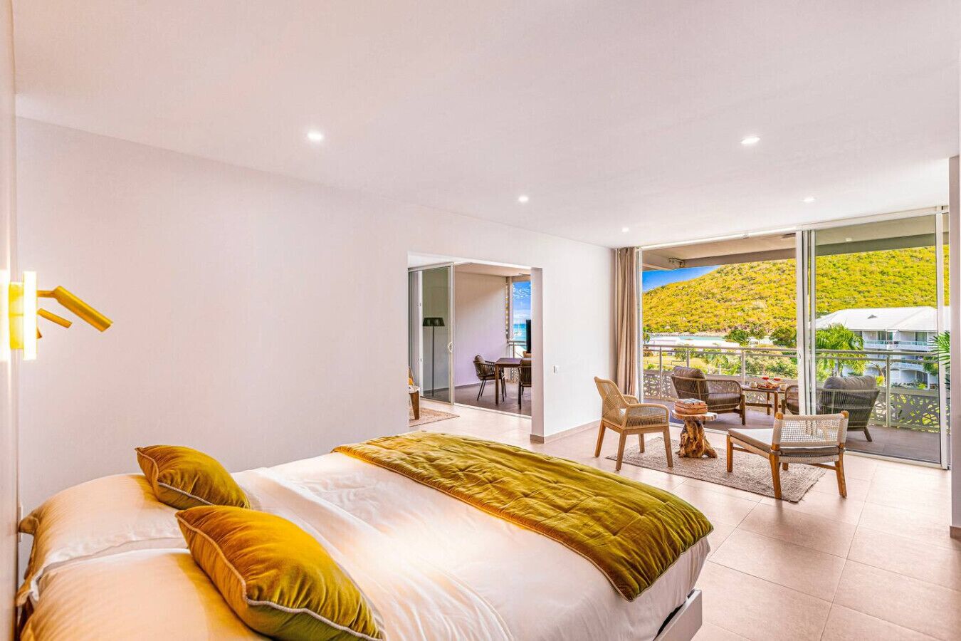 Une chambre moderne avec un grand lit, un balcon aménagé avec des sièges et une vue sur une colline.