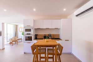 A modern kitchen with white cabinets, a wooden dining table, and a built-in oven. - Prestigious Serenity Bay beachfront suite (Anse Marcel)