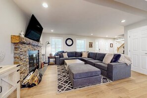 Ein Wohnzimmer mit Kamin aus Stein, einem großen Ecksofa, einem Flachbildfernseher und einer Treppe zu einer weiteren Ebene.