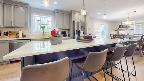 Una cocina moderna con una isla grande, taburetes de bar, iluminación colgante y vistas al área de comedor.