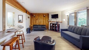 A modern living room with a wooden accent wall, a sofa, a TV, and a bar area with stools.