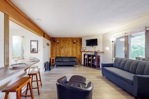 Ein modernes Wohnzimmer mit einer Wand in Holzoptik, einer Couch, einem Fernseher und einer Bar mit Hockern.