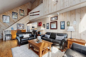Ein gemütliches Wohnzimmer mit einer Holztreppe, Ledersofas, einem Holztisch und verschiedenen gerahmten Bildern an den Wänden.