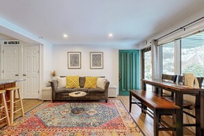 Una habitación con sofá, una mesa de comedor, un tapete estampado y un ventanal con cortinas.