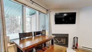 Un coin repas avec une table et des chaises en bois, une cheminée et un téléviseur fixé au mur.