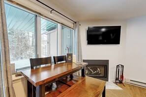 Un comedor con mesa y sillas de madera, una chimenea y un televisor montado en la pared.