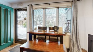 Une pièce avec une table et des chaises en bois, une fenêtre avec des rideaux et une porte.