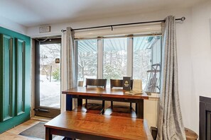 Una habitación con una mesa y sillas de madera, una ventana con cortinas y una puerta.