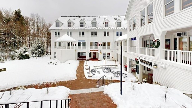 Un bâtiment blanc doté de nombreuses fenêtres, d’une entrée centrale et d’un espace extérieur abrité aménagé en coin salon.