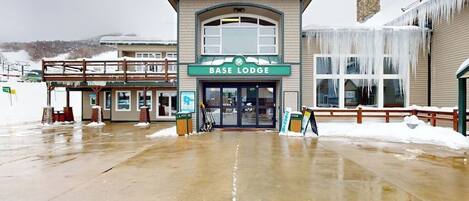 A building labeled 'BASE LODGE' with a snow-covered ground and a wooden fence.