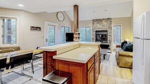 Una cocina amplia con una isla central, un comedor con una mesa larga y sillas, una sala de estar con sofá y una chimenea de piedra.
