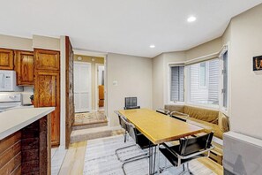 A compact kitchen with wooden cabinets, a dining table with chairs, a built-in oven, and a window with blinds. - All-season landing pad with resort amenities, mtn views, & W/D - dog-friendly (Waterville Valley)