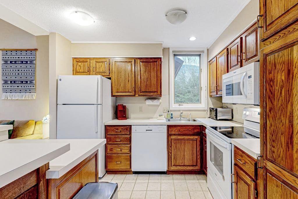 A compact kitchen with wooden cabinets, a white refrigerator, a dishwasher, a microwave, and a stove.