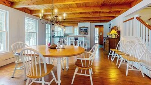 Un coin repas avec une table en bois et des chaises blanches, une cuisine en arrière-plan et un escalier menant à un autre niveau.