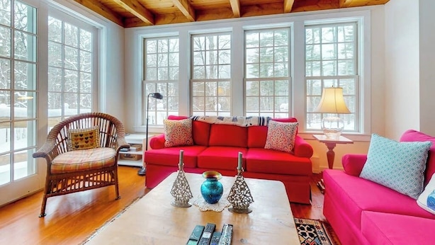 Un salon chaleureux avec un canapé rouge, un fauteuil en osier et une table basse agrémentée d’objets décoratifs.