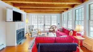 Un salon chaleureux avec une cheminée, un canapé rouge, un téléviseur et de grandes fenêtres.